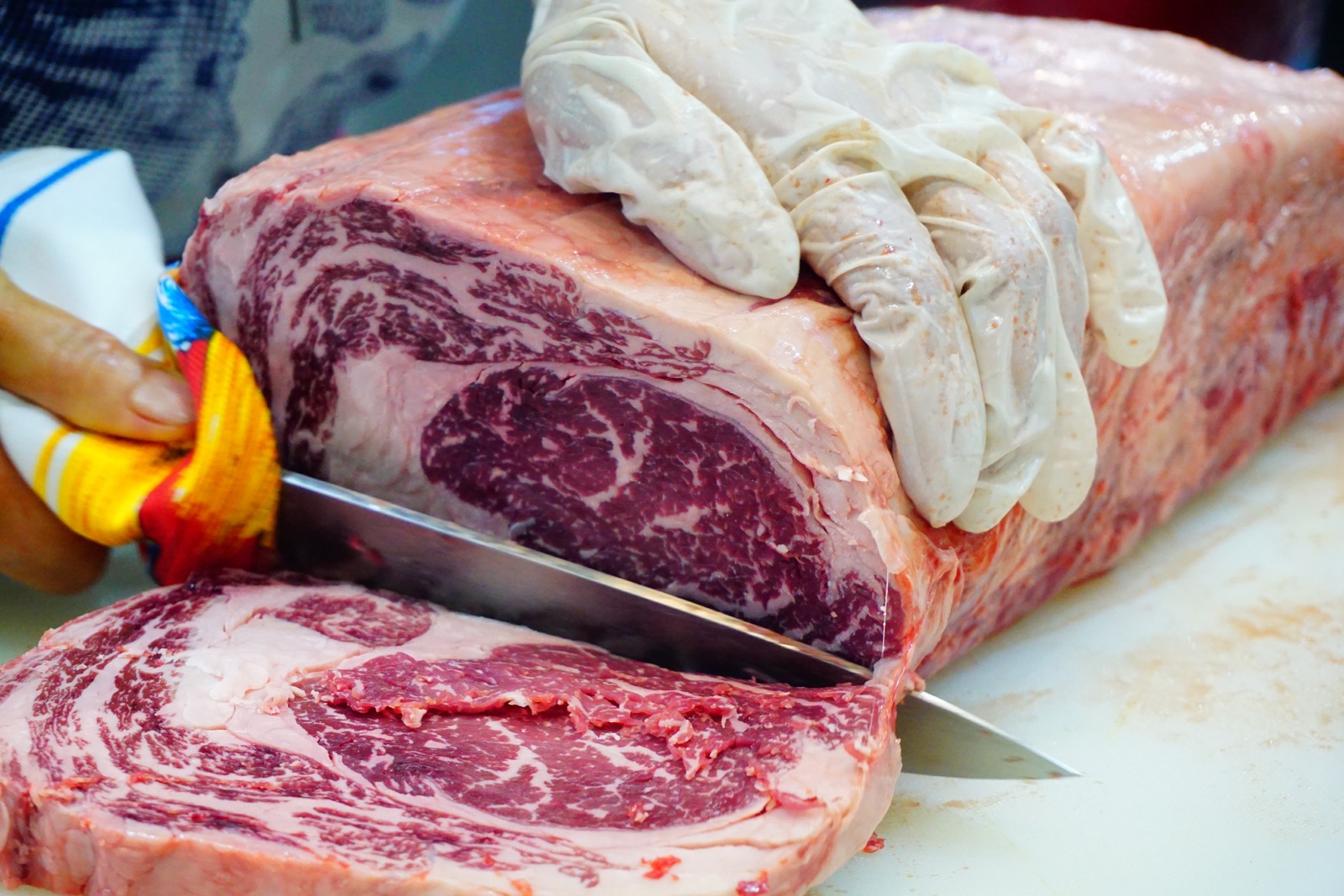 A whole Wagyu cube roll on a butcher block, part-way through being cut into steaks
