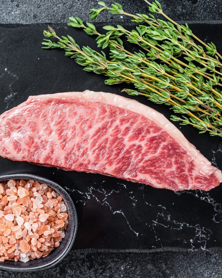 A raw marbled steak on dark slate with thyme and salt