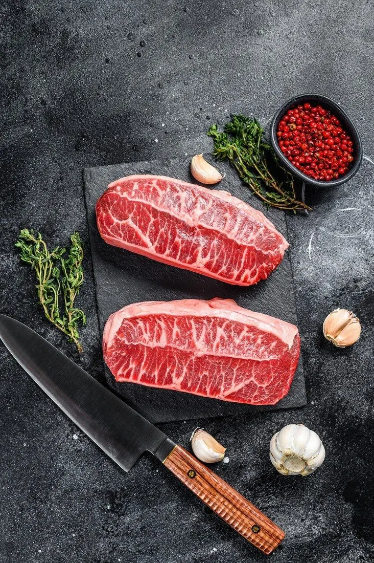 Two thick raw marbled steaks on dark slate